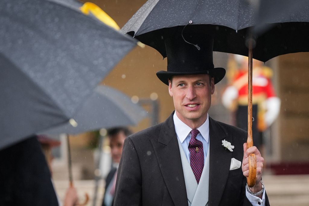 Britain's Prince William is wearing a hat and hiding under an umbrella 