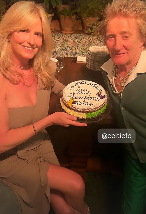 Penny Lancaster in a brown dress holding a cake and with her is Rod Stewart in a green dress