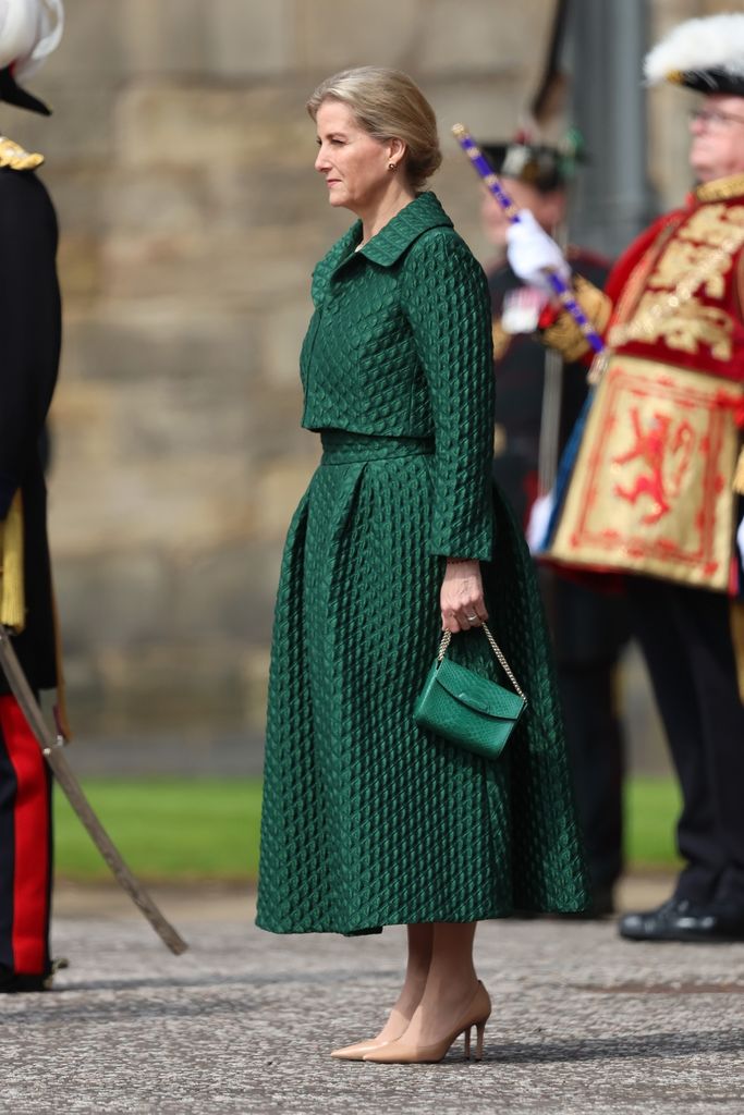 Sophie stands at attention in a green skirt and jacket