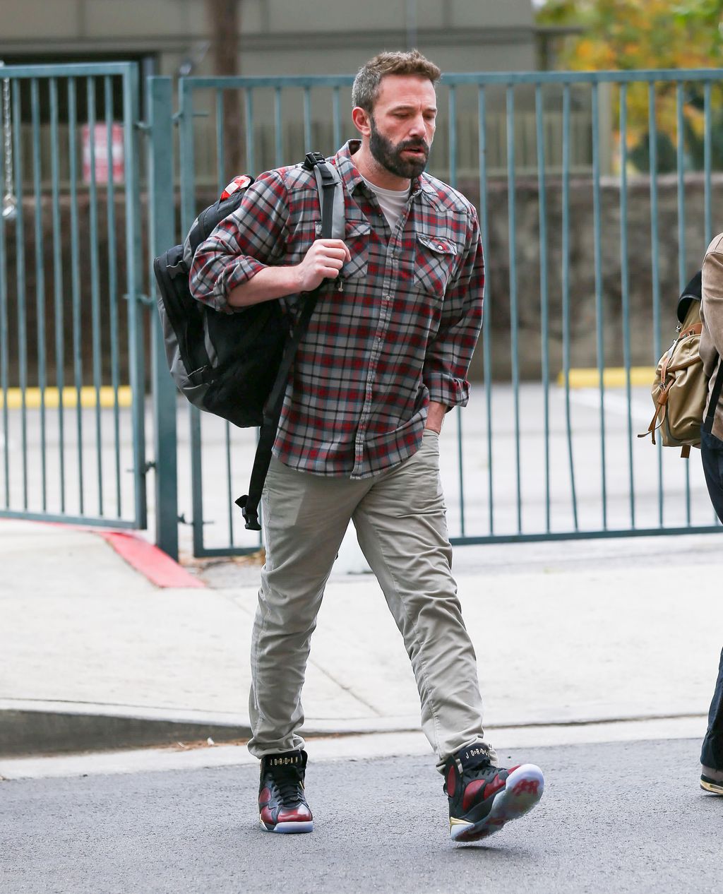 Ben Affleck wearing a normcore staple, some baggy trousers, a plaid shirt, sneakers, and a backpack