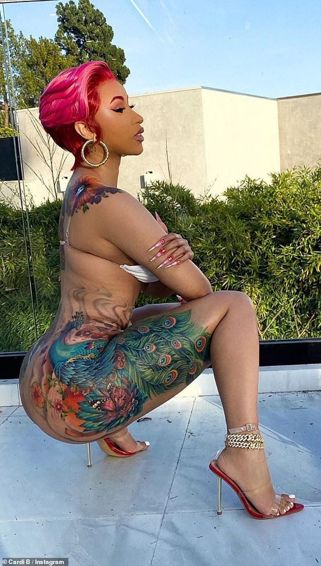 Rapper Cardi B shows off her detailed and dazzling thigh tattoos while posing in a white bra top