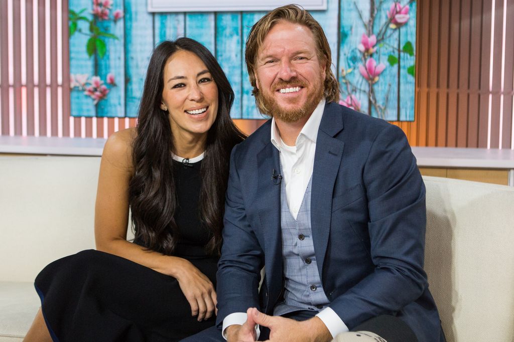 Chip Gaines in blue suit and Joanna Gaines in black dress smiling on TV