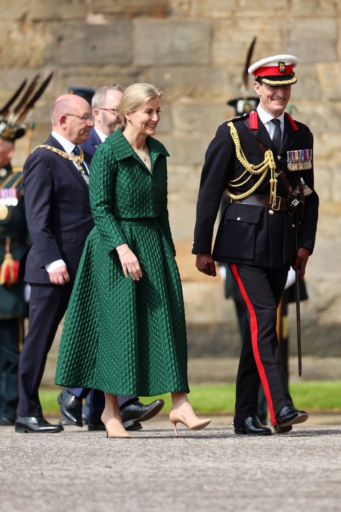 Sophie, dressed in green, is walking with a man in uniform. 