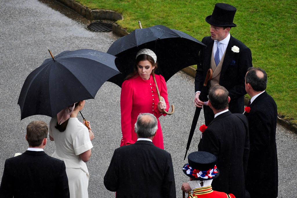 Princess Beatrice wearing a red dress and headband at the Buckingham Palace garden party in the rain