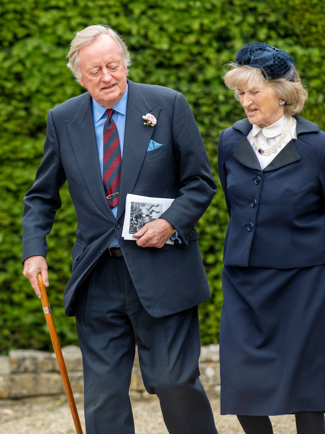 Andrew Parker Bowles walking with the help of a stick and a woman
