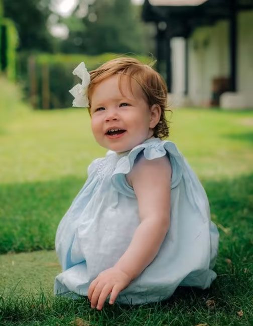one year old lilibet sits on grass wearing a light blue dress and matching bow in her hair