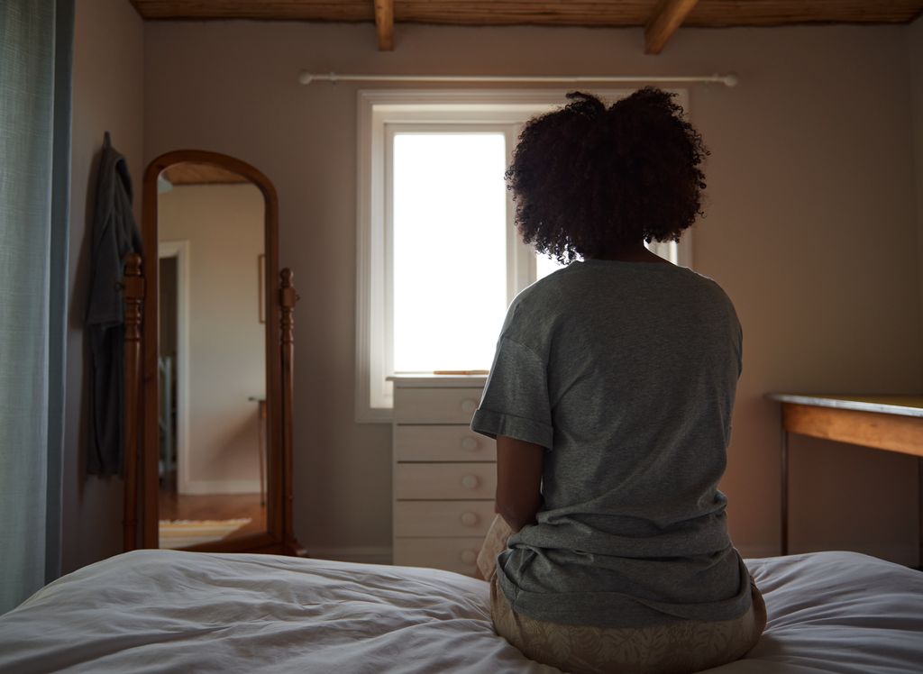 Rear view of a young woman sitting on her bed and looking out the window