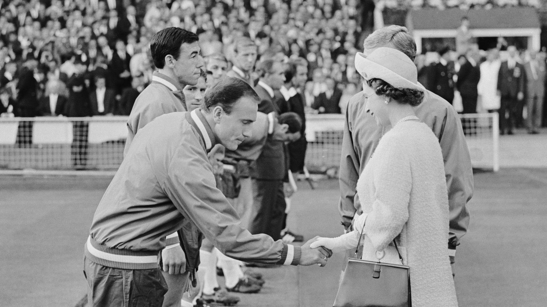 Black and white photo of the late Queen shaking hands with members of the 1966 England World Cup team
