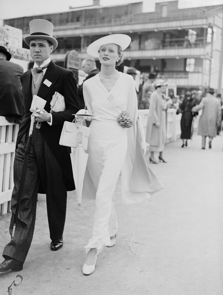 UNITED KINGDOM - NOVEMBER 07: COUPLE AT ROYAL ASCOT, 1935. Photograph of a couple walking through racegoers at the Royal Hunt Cup horse race, taken by Edward Malindin for the Daily Herald newspaper on June 19, 1935. The woman is seen in an elegant white dress, while her companion wears a top hat and tails - traditional dress in the 1930s. The racecourse at Royal Ascot was founded in 1711 by Queen Anne. As a racecourse favoured by British royalty, Ascot has become a highlight of the social season and is famous for its fashion, particularly its hats. This photograph is selected from the Daily Herald archive, which contains more than three million photographs. The archive contains work of international, national and local significance by staff and agency photographers. (Photo: Daily Herald Archive/SSPL/Getty Images)