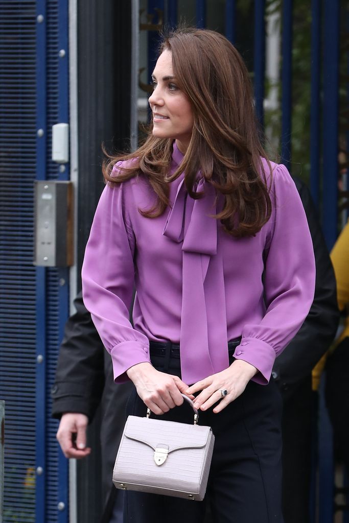 Princess Kate wearing a purple blouse and carrying a lilac bag