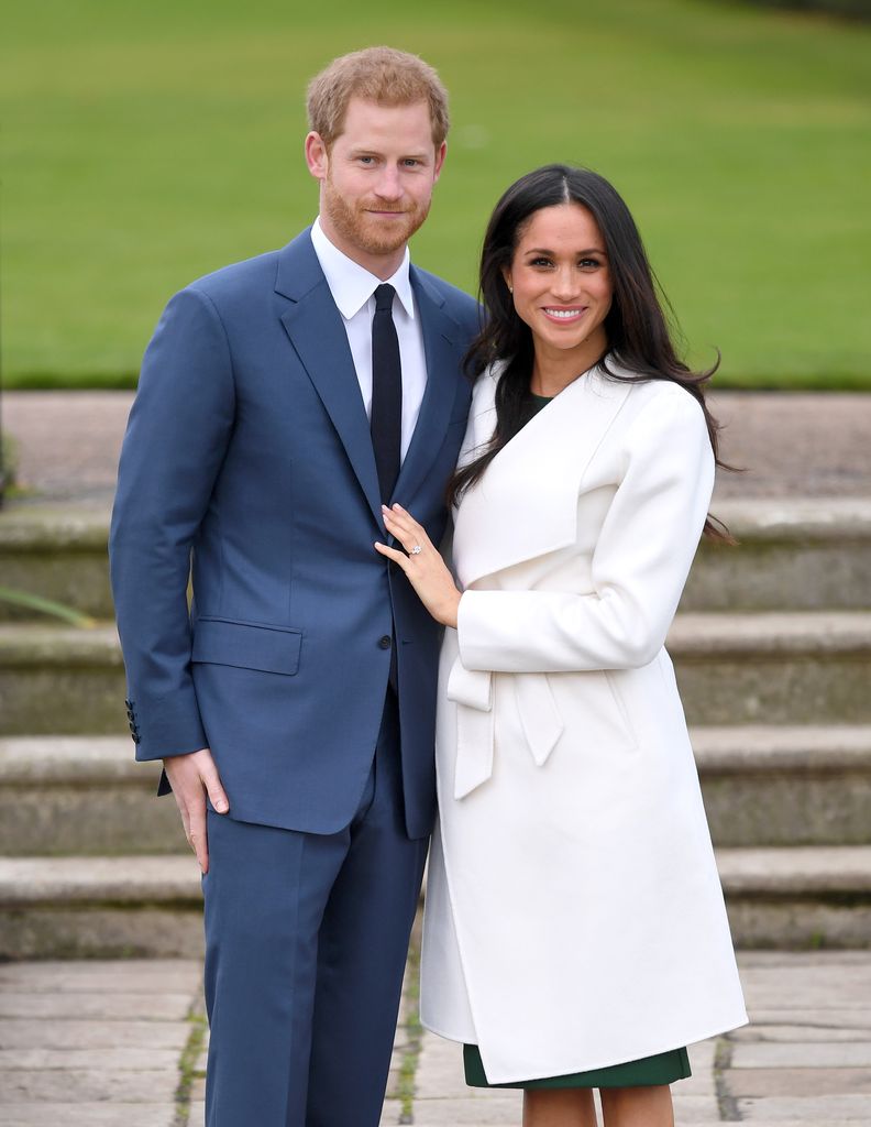 Prince Harry in a blue suit and Meghan Markle in a white overcoat