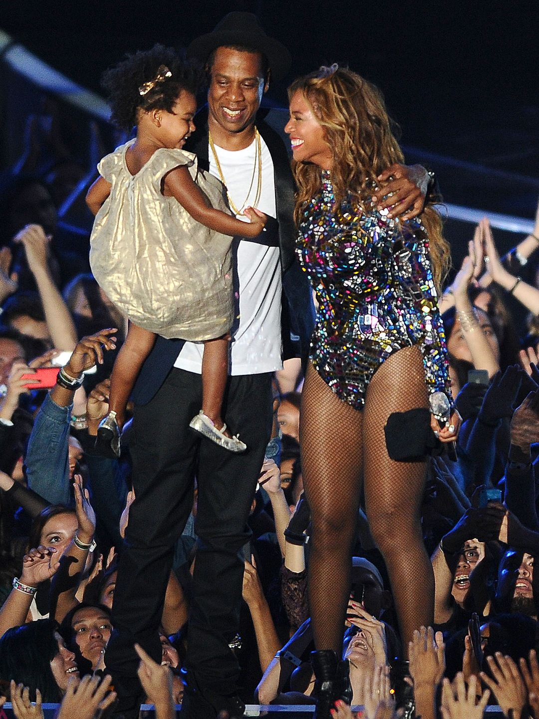 Beyoncé and Jay-Z stand smiling on stage, with Jay-Z holding Blue Ivy in his arms