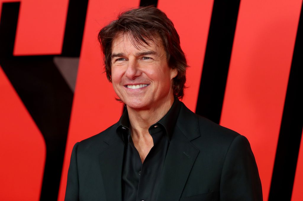 Tom Cruise smiling on the red carpet in a black suit 