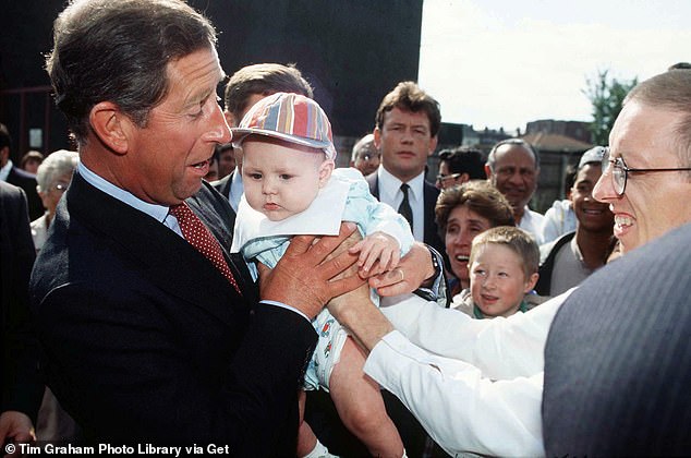 King Charles, then the Prince of Wales, looks surprised as a baby is thrust into his arms during a visit to a housing development in an inner city area of Birmingham in 1995