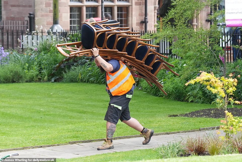 A workman carries a bundle of chairs through the garden at Chester Cathedral