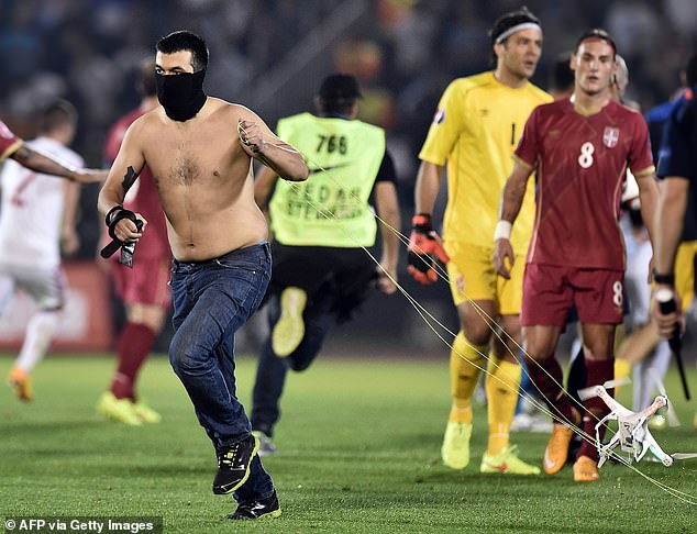A masked Serbian supporter runs away with a drone carrying the controversial flag while players watch in the background