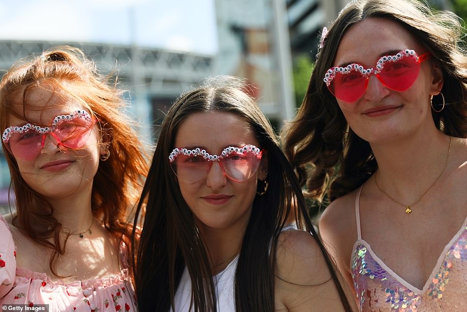Three girls wear personalised pink heart sunglasses that read 'The Eras Tour - London N1'
