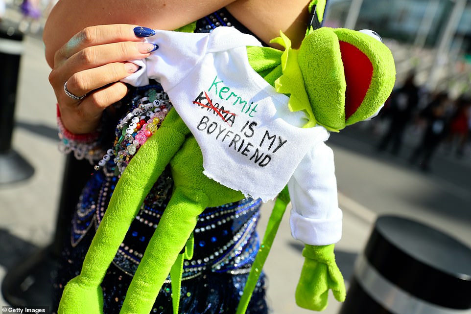 A fan carries a Kermit toy wearing a shirt with the words 'Kermit is my boyfriend', a play on Swift's lyrics 'Karma is my boyfriend'