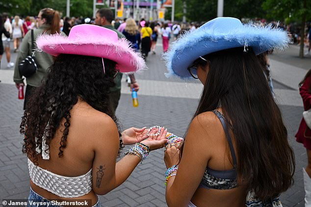 A pair of Swifties wearing pink and blue cowboy hats look at bracelets as they wait for the concert to begin