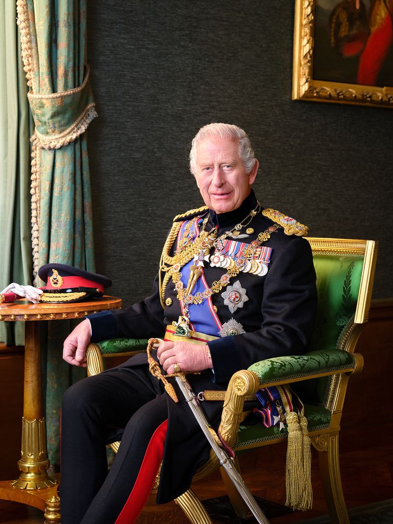 King Charles sits on a green chair in a black military uniform