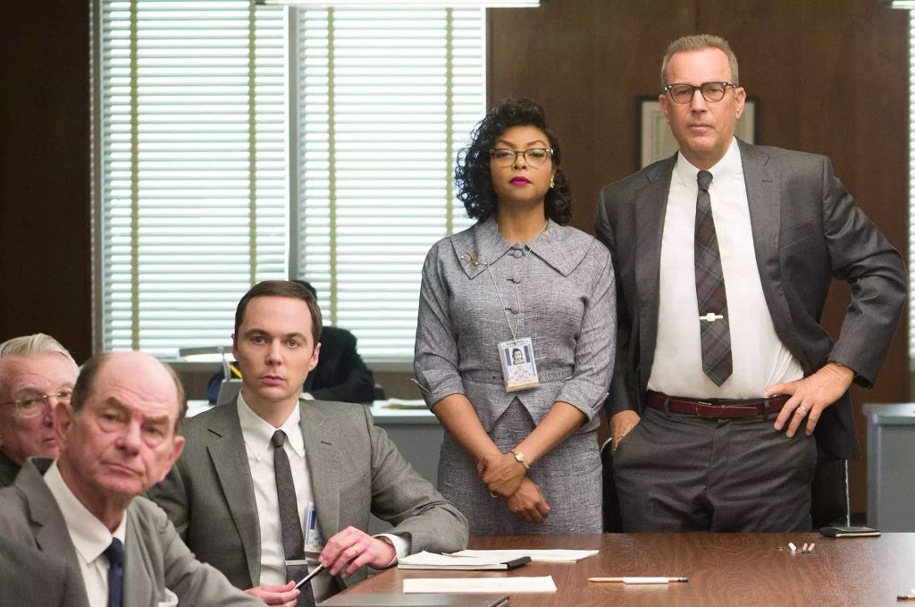Kevin Costner (far right) with Taraji P Henson (center) and Jim Parsons (left) in Hidden Figures. Jim is seated at a large table and Taraji and Kevin are standing.