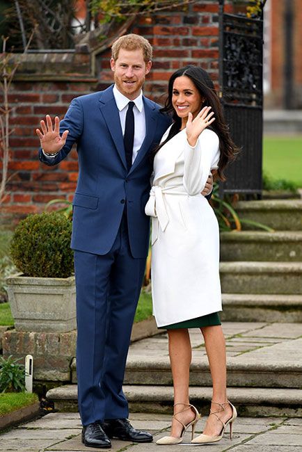 harry wears a blue suit and wraps his arm around meghan who wears a white coat as they wave at cameras