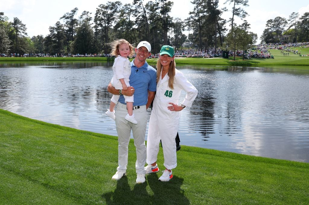 Rory McIlroy and his wife Erica Stoll hold a little girl in their arms as they stand in front of a lake on a golf course