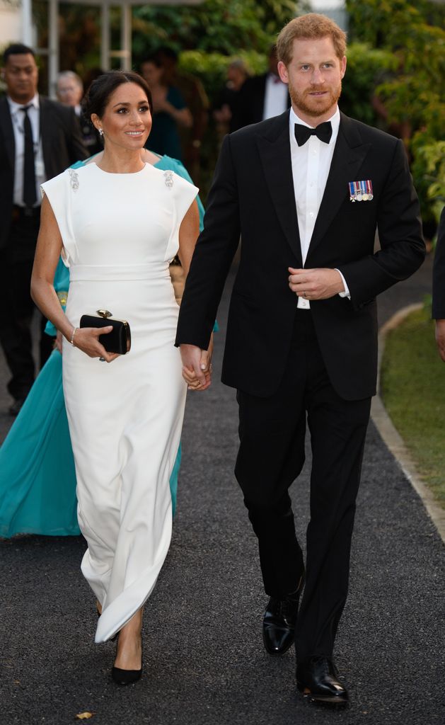 The Duchess of Sussex in a white dress holding Prince Harry's hand