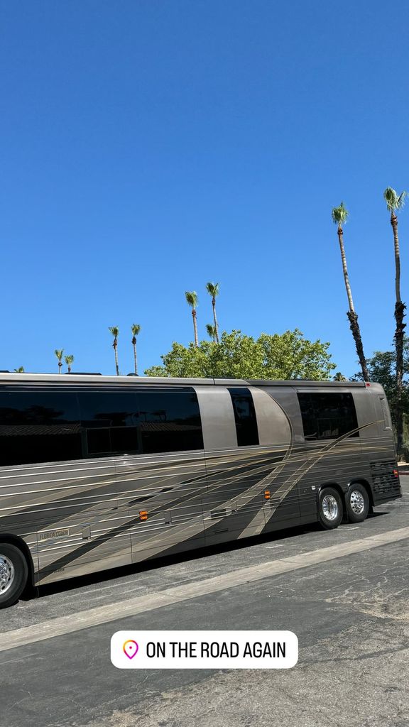 Posted by Kourtney Kardashian, A large tour bus is parked in a parking lot with palm trees behind it 